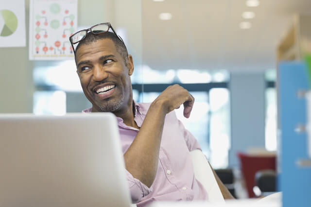 Businessman sitting at a desk, smiling, with glasses on his head.