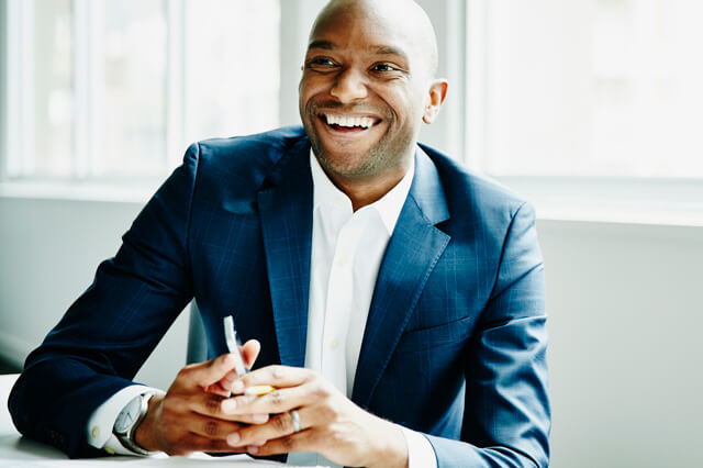 Businessman smiling with windows behind him.