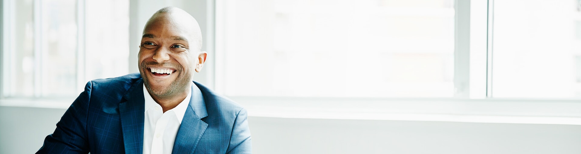 Businessman smiling with windows behind him.