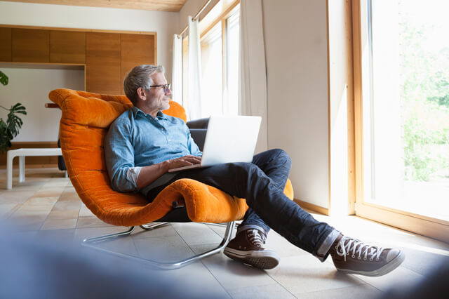 Middle-aged man sitting in a chair using a laptop.