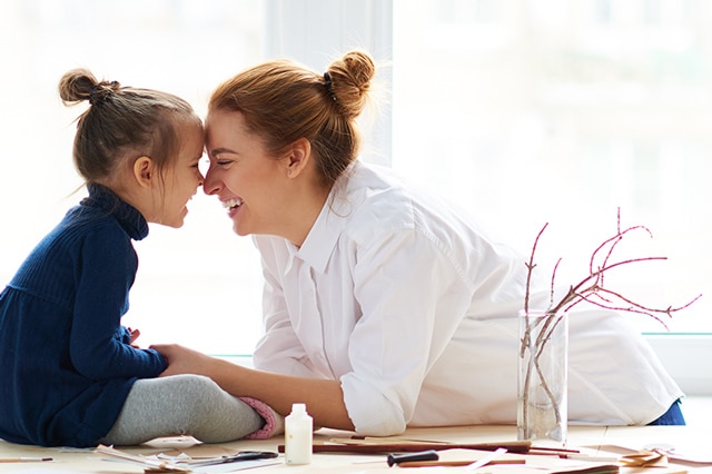 Mother and daughter smiling at each other and touching noses.