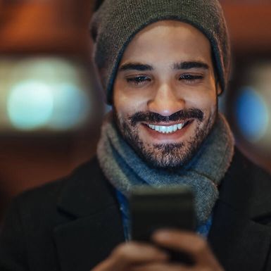 Young man in winter attire uses a smartphone.