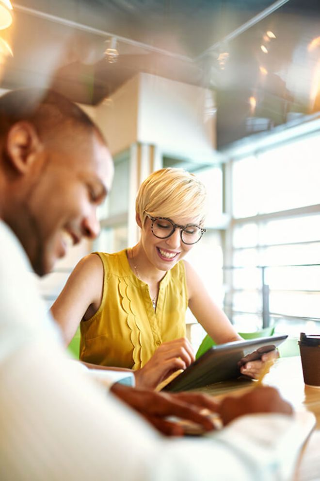 A young woman uses a tablet while a man smiles in the foreground.