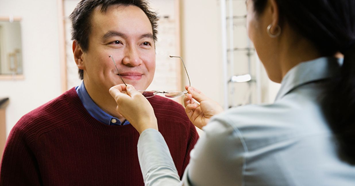An eye doctor helping a man try on glasses.