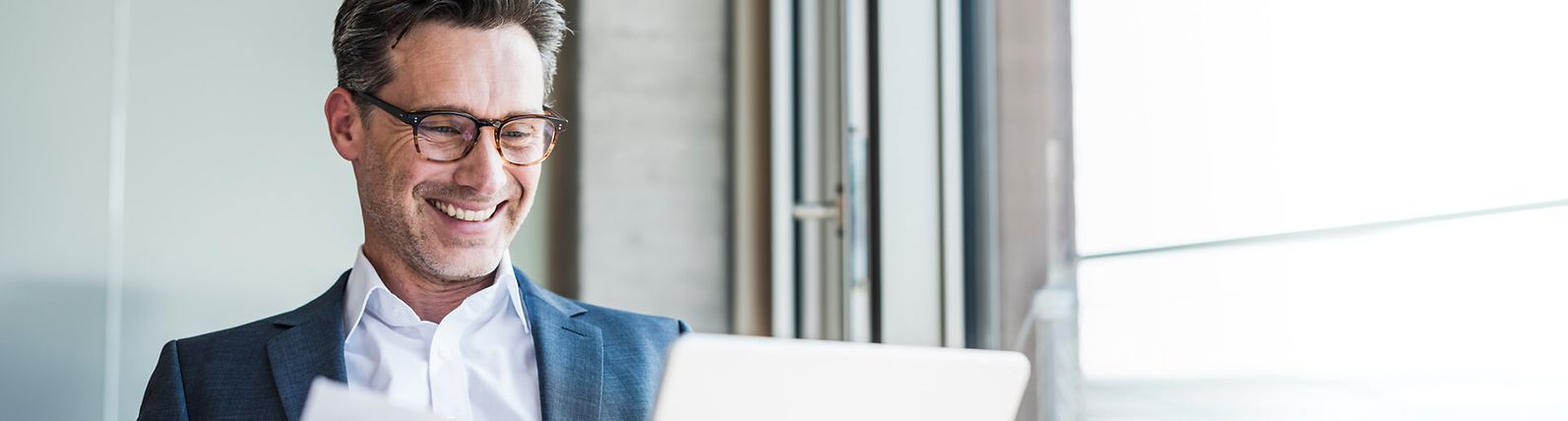 Businessman with glasses smiling and using a laptop.