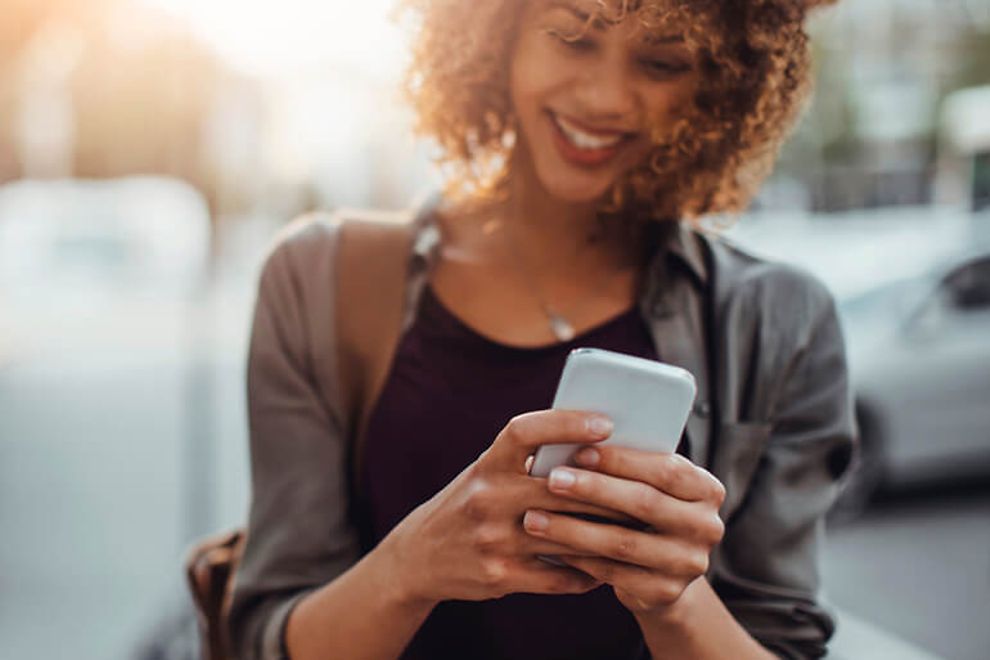 Young woman using smartphone, walking outdoors, smiling.