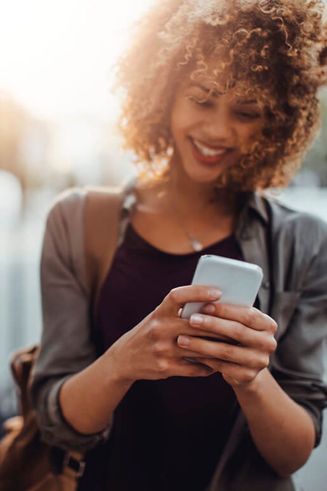 Young woman using smartphone, walking outdoors, smiling.