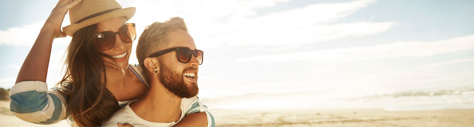 Young couple with sunglasses smiling on a beach.