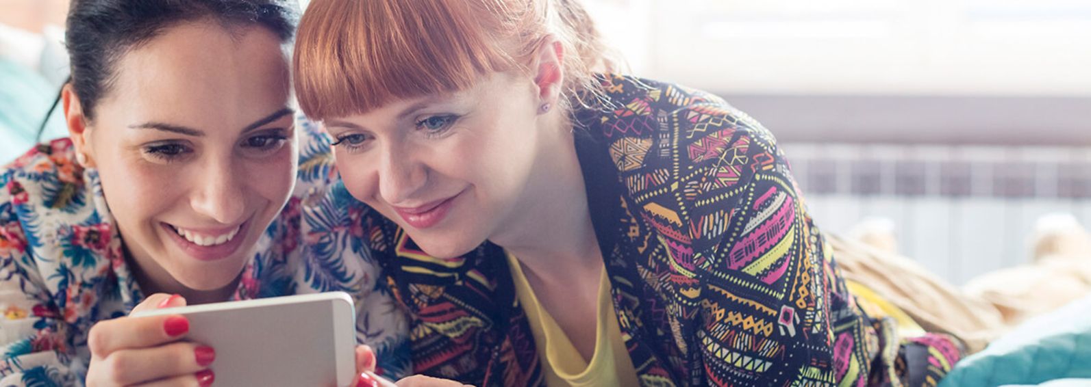 Two young women looking at a phone together and smiling.