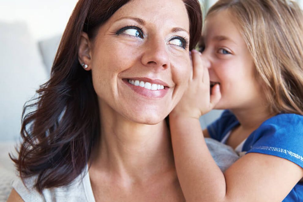 A young girl whispering in her mother's ear