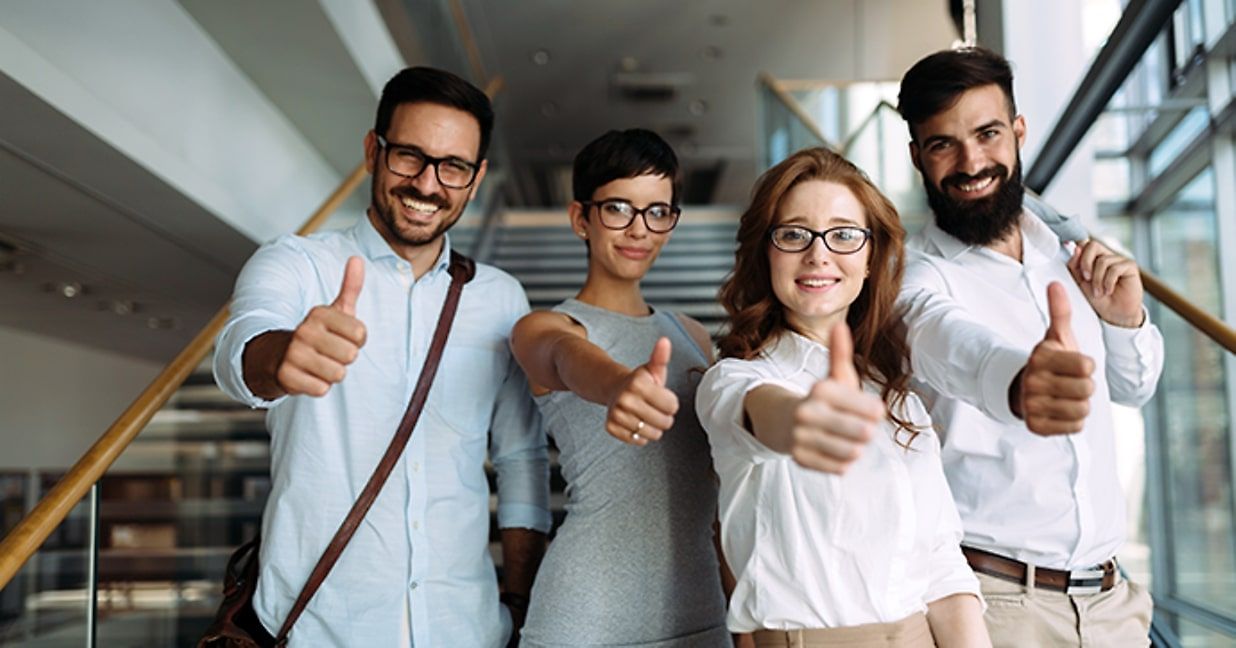 four employees, standing at the bottom of a staircase, all wearing white business-casual shirts 